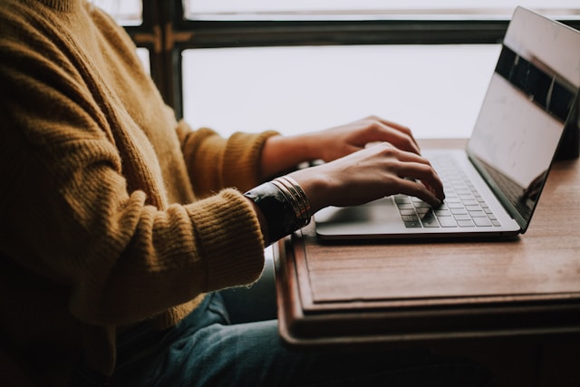 Close-up of a person in a yellow sweater typing on a laptop.